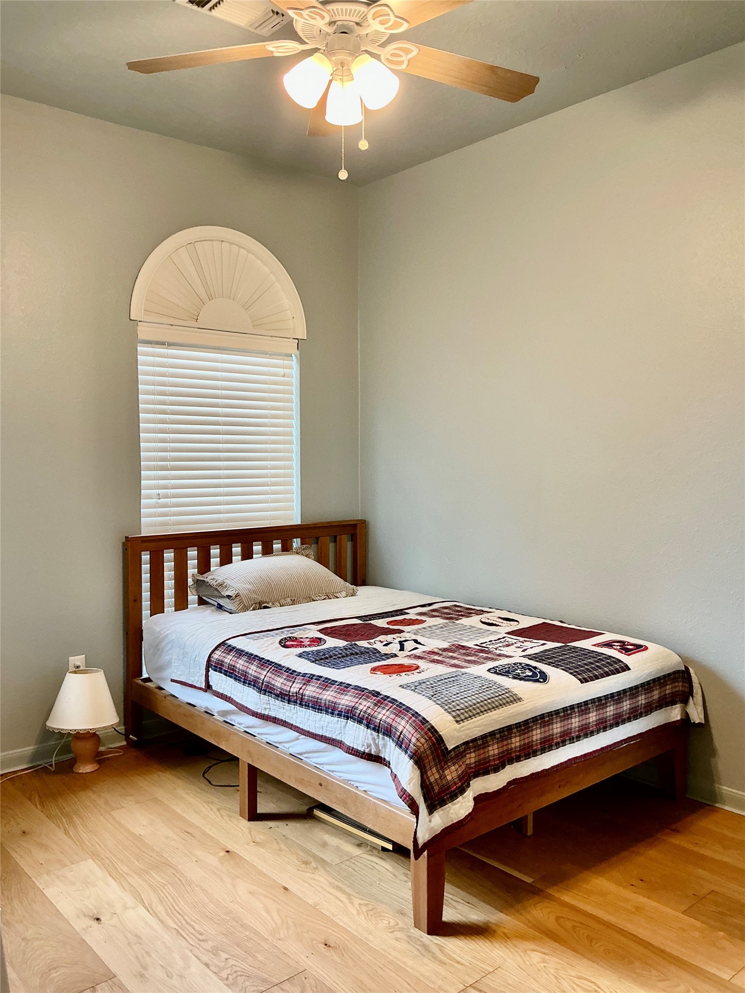 2910 Crescent Bend Road Spring, TX 77388 - Photo 18 of 29 This cozy bedroom features a wooden bed with a patchwork quilt, light wood flooring, and a ceiling fan. A window with a decorative arch lets in natural light, complemented by soft, neutral wall colors.