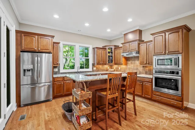 a kitchen with stainless steel appliances granite countertop a refrigerator a stove a sink a dining table and chairs with wooden floor