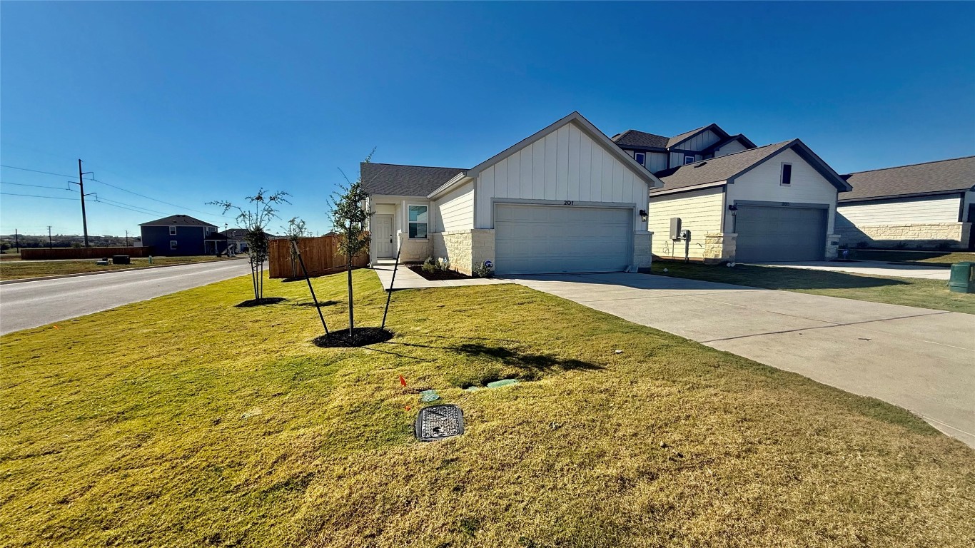201 Firefox Way Jarrell, TX 76537 - Photo 2 of 27 View of front facade featuring board and batten siding, concrete driveway, a front lawn, an attached garage, and stone siding