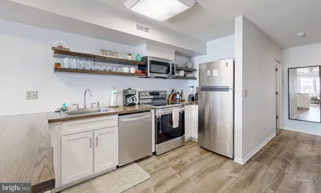 a kitchen with stainless steel appliances granite countertop a refrigerator a sink a stove and white cabinets with wooden floor