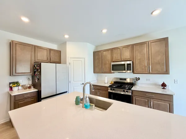 a large kitchen with stainless steel appliances a refrigerator a stove a sink a center island and couches