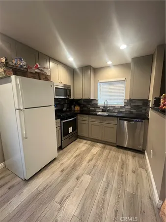 a kitchen with granite countertop a refrigerator a sink and dishwasher a oven with wooden floors