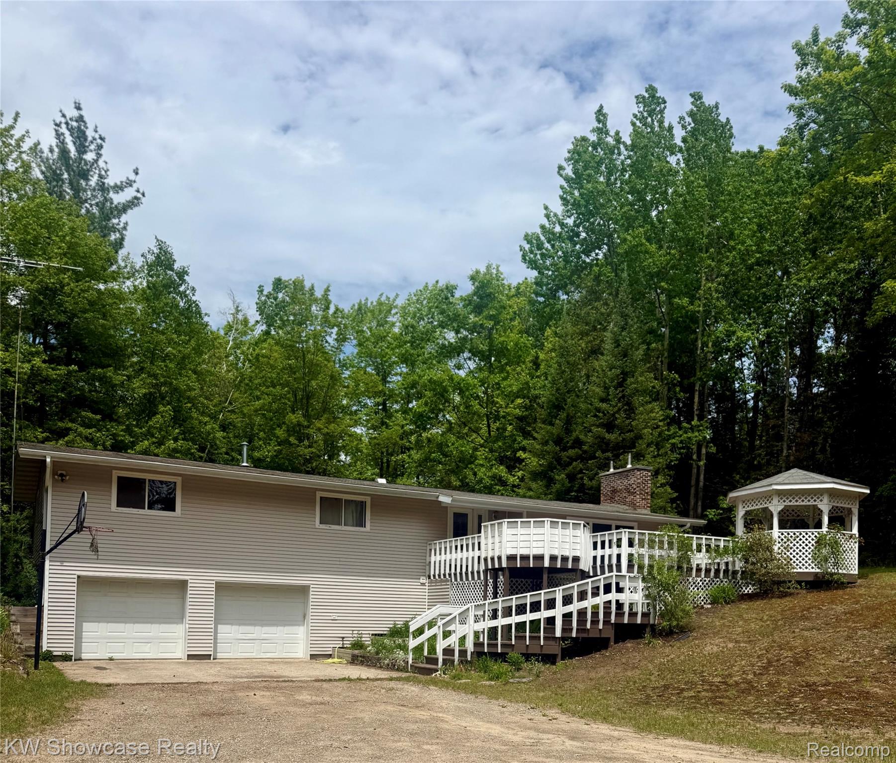 Ranch-style residence featuring a two-car garage, expansive multi-level deck with white railings, and an attached white gazebo