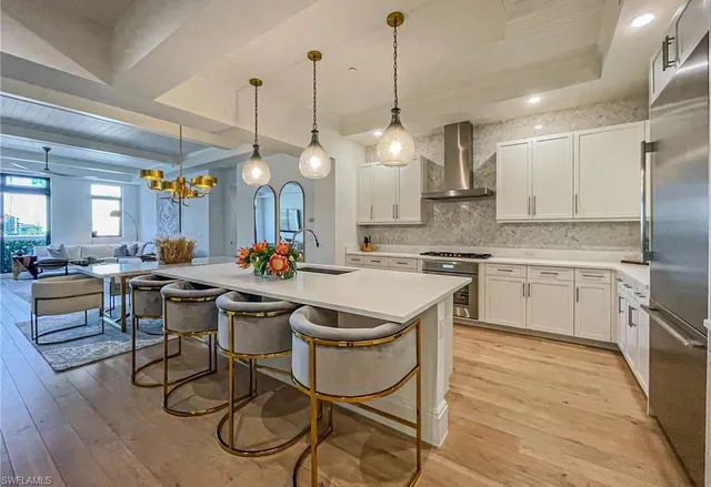 a open kitchen with stainless steel appliances granite countertop a stove a sink dishwasher a dining table chairs with white cabinets and wooden floor