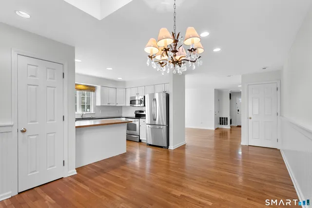 a view of a kitchen with stainless steel appliances granite countertop a refrigerator a sink dishwasher a stove and white cabinets with wooden floor