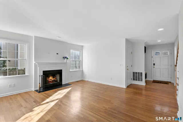 a view of an empty room with wooden floor fireplace and a window