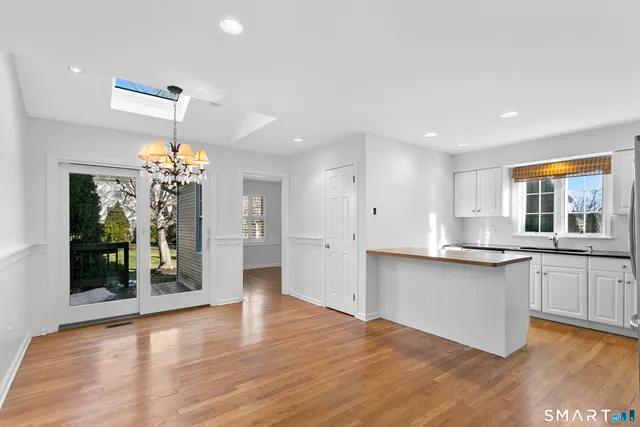 a kitchen with stainless steel appliances granite countertop a refrigerator a sink dishwasher a stove and white cabinets with wooden floor