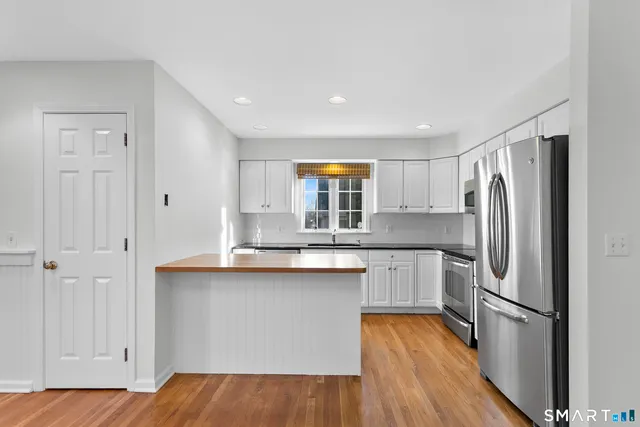 a kitchen with stainless steel appliances granite countertop a refrigerator a sink dishwasher a stove and white countertops with wooden floor