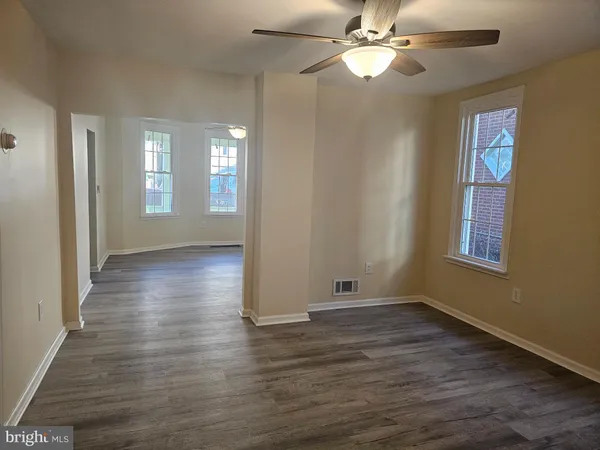 an empty room with wooden floor fan and windows