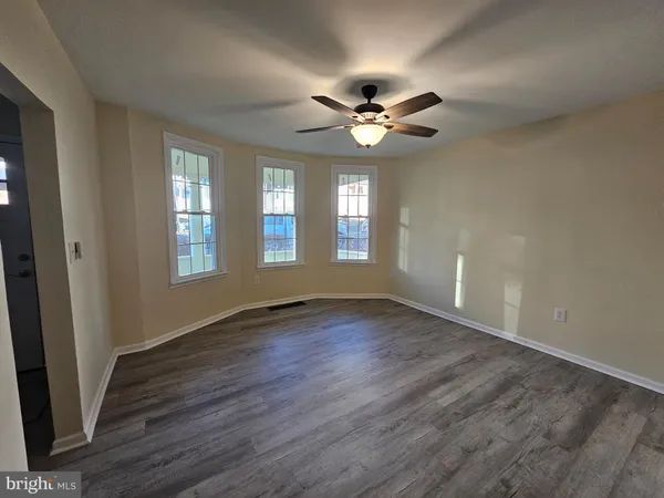 an empty room with wooden floor fan and windows