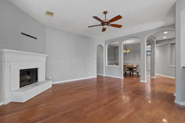 a view of an empty room with chandelier fan and wooden floor
