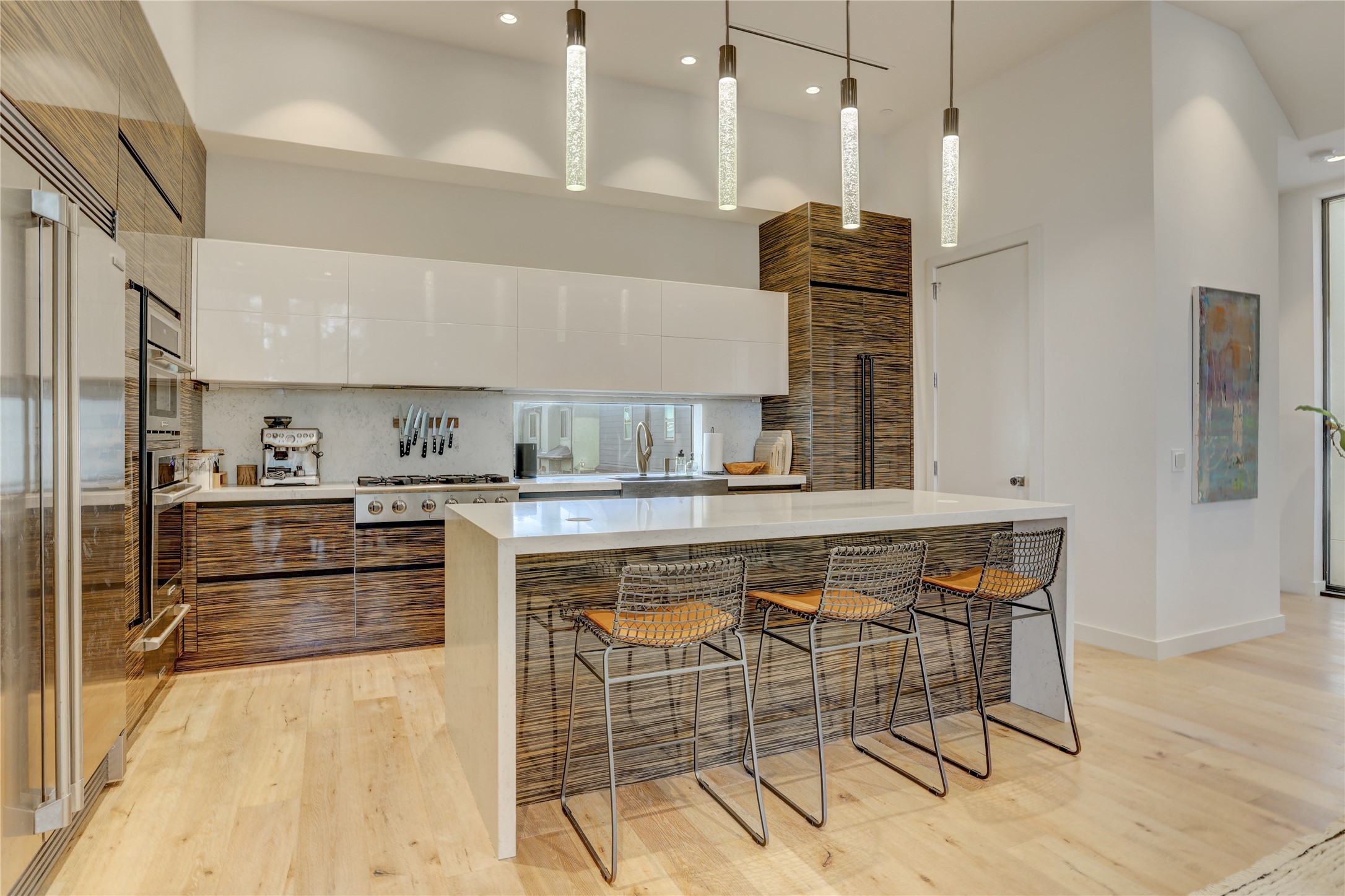 1807 Indiana Street Houston, TX 77006 - Photo 12 of 35 Chef’s Kitchen: Gourmet kitchen showcasing high-gloss white upper cabinets paired with exotic linear-grain lower cabinetry, premium integrated Electrolux ICON appliances, a window backsplash, and a quartz waterfall island with bar seating.