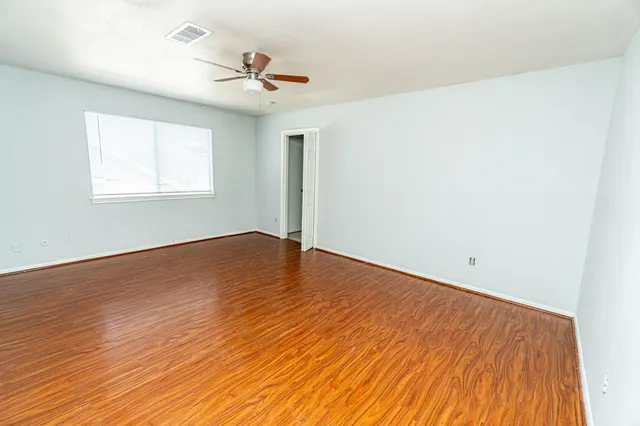 a view of empty room with wooden floor and fan