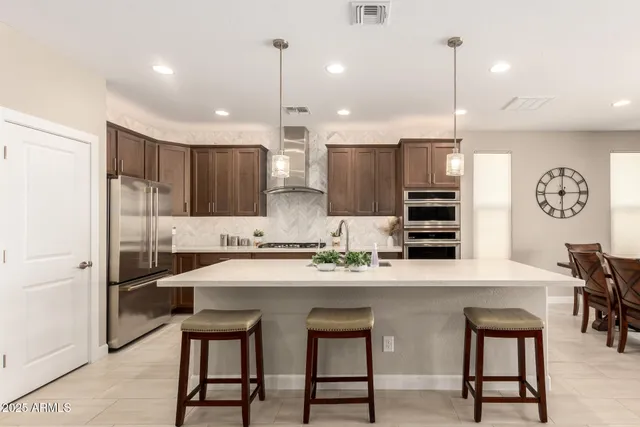 a kitchen with stainless steel appliances kitchen island granite countertop a sink a stove a refrigerator and chairs