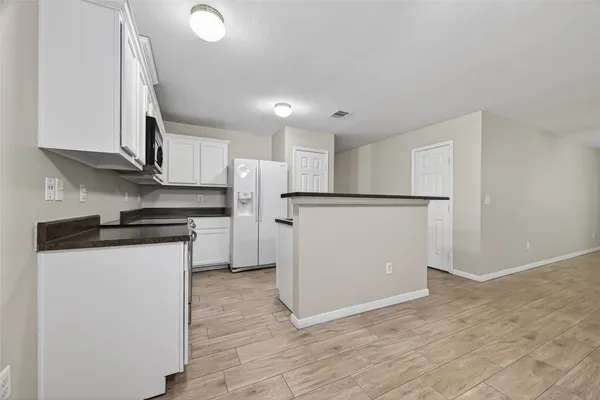 a kitchen with stainless steel appliances granite countertop a refrigerator a stove a sink and white cabinets with wooden floor