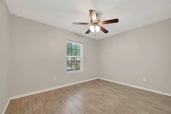 an empty room with wooden floor fan and windows