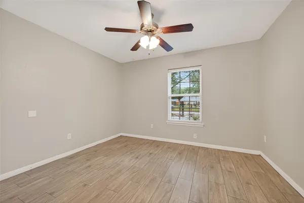 an empty room with wooden floor chandelier fan and windows