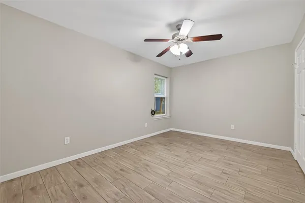 a view of an empty room with wooden floor and a ceiling fan