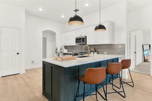 a kitchen with stainless steel appliances granite countertop a sink a stove a kitchen island with chairs and white cabinets