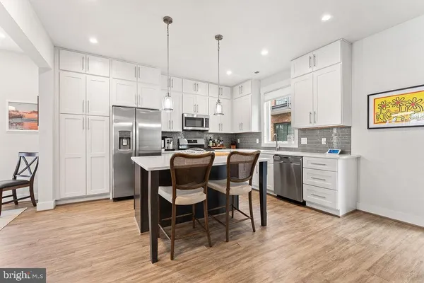 a kitchen with stainless steel appliances granite countertop a stove top oven a refrigerator a dining table and chairs with wooden floor