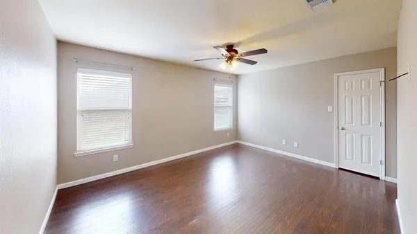 an empty room with wooden floor fan and windows