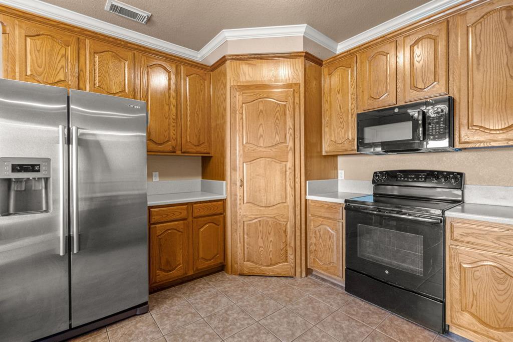 6501 Indian Trail Sanger, TX 76266 - Photo 11 of 40 Kitchen with black appliances, ornamental molding, light countertops, light tile patterned floors, and a textured ceiling