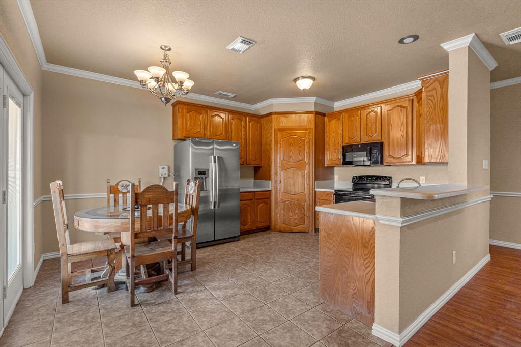 6501 Indian Trail Sanger, TX 76266 - Photo 8 of 40 Kitchen featuring light countertops, crown molding, black appliances, a chandelier, and brown cabinetry