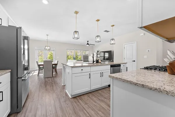 a kitchen with stainless steel appliances kitchen island granite countertop a refrigerator a stove a sink and white cabinets with wooden floor