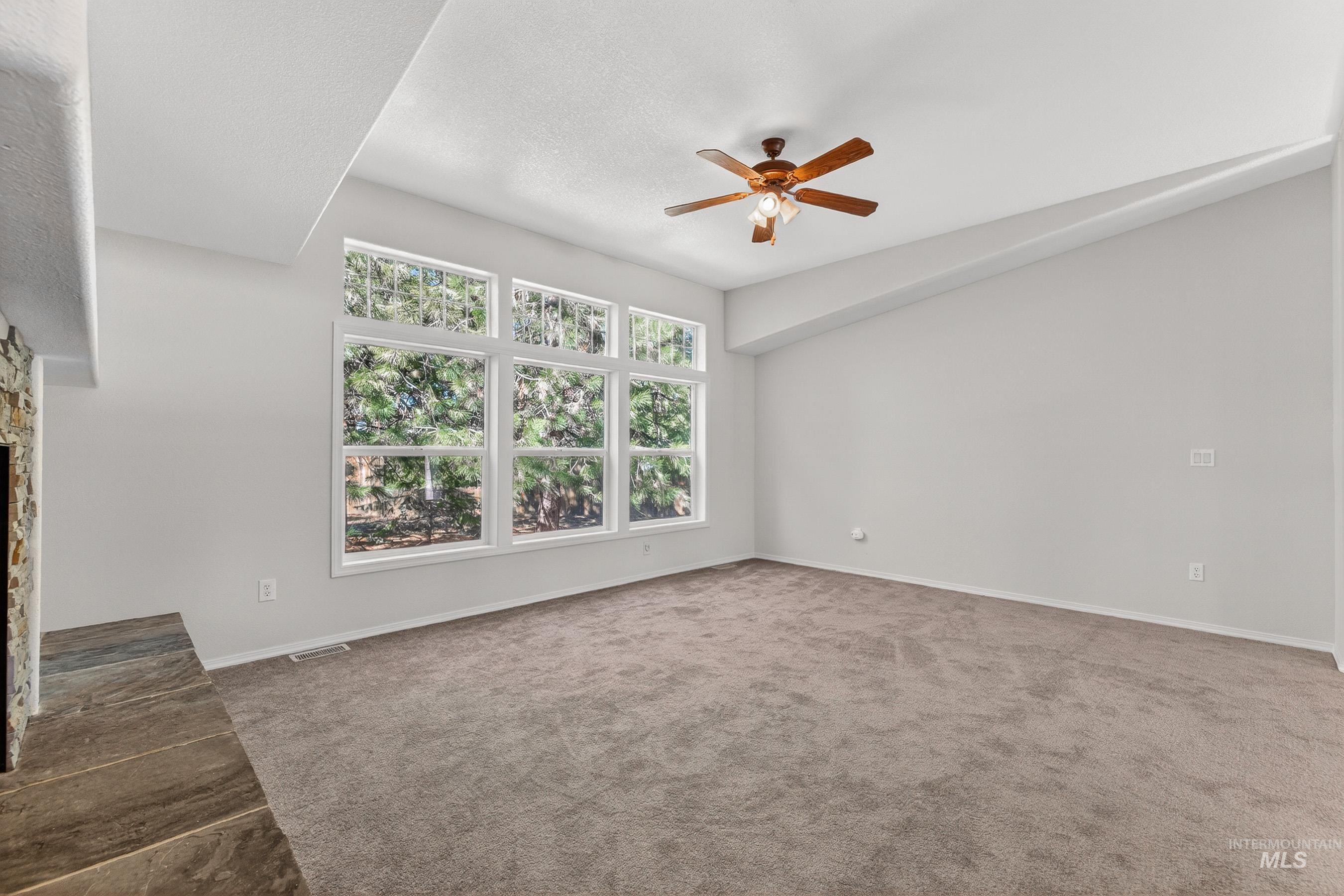 1649 Crown Point Parkway Cascade, ID 83611 - Photo 12 of 24 Spacious room featuring a stone fireplace with a slate hearth, expansive window array, vaulted ceiling, and ceiling fan