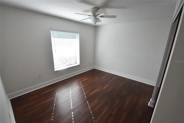 an empty room with wooden floor chandelier fan and windows