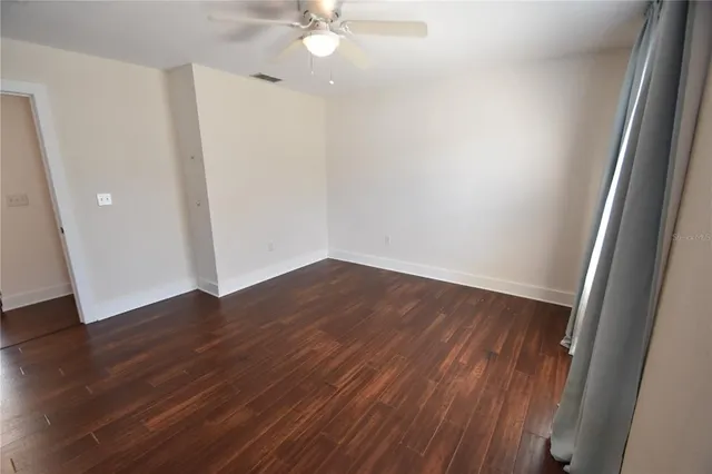 an empty room with wooden floor and fan