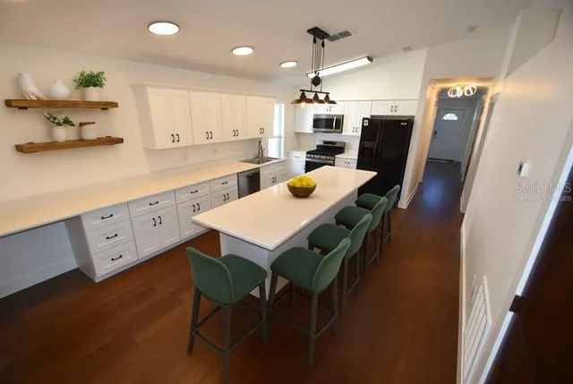 a kitchen with stainless steel appliances kitchen island granite countertop a table chairs sink and white cabinets