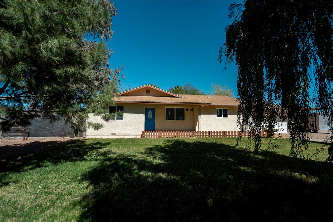 The property features a stucco exterior with a light brown roof, a blue front door, and a picket fence