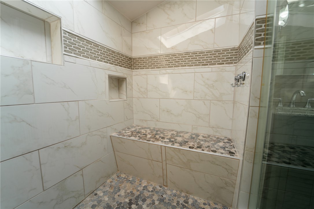 1985 Laguna Road Mohave Valley, AZ 86440 - Photo 32 of 83 The shower features light-colored marble-look tile walls with a decorative accent band, a built-in bench with pebble-style tiling, and a recessed niche for storage
