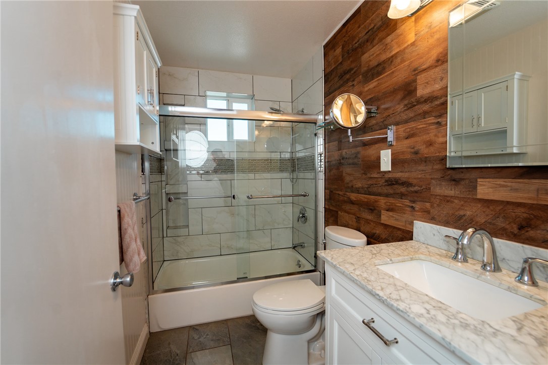1985 Laguna Road Mohave Valley, AZ 86440 - Photo 42 of 83 The bathroom features a vanity with a white countertop and sink, a mirror with an integrated light fixture, a toilet, and a bathtub with a glass enclosure