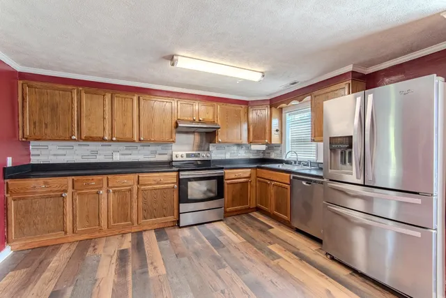 a kitchen with stainless steel appliances granite countertop a refrigerator a sink dishwasher a stove with wooden cabinets and floor