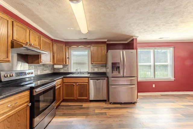 a kitchen with stainless steel appliances granite countertop a refrigerator a sink dishwasher a stove with wooden cabinets and floor