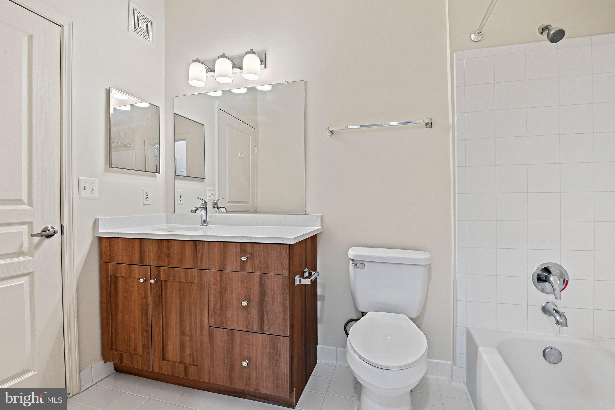 12001 Market Street, Unit 151 Reston, VA 20190 - Photo 15 of 25 a bathroom with a toilet a sink a mirror a vanity and bathtub