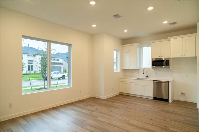 a large kitchen with stainless steel appliances granite countertop a stove a sink white cabinets and a wooden floor