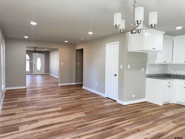 an empty room with wooden floor and kitchen view