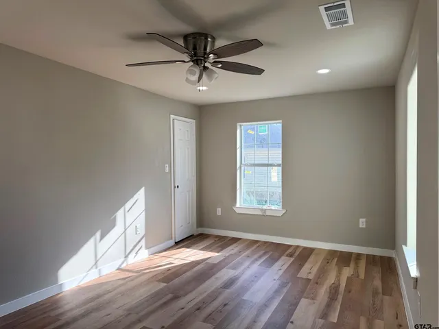 an empty room with wooden floor fan and windows