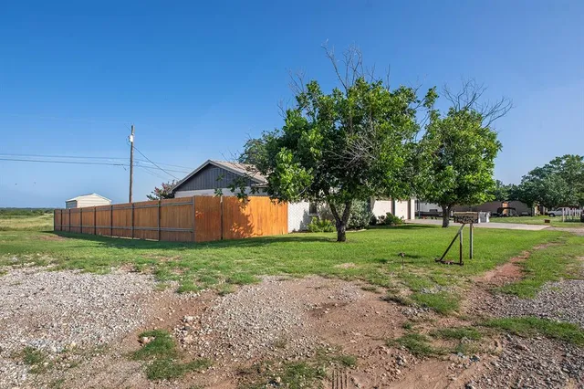 a view of a yard in front of a house with plants and large tree