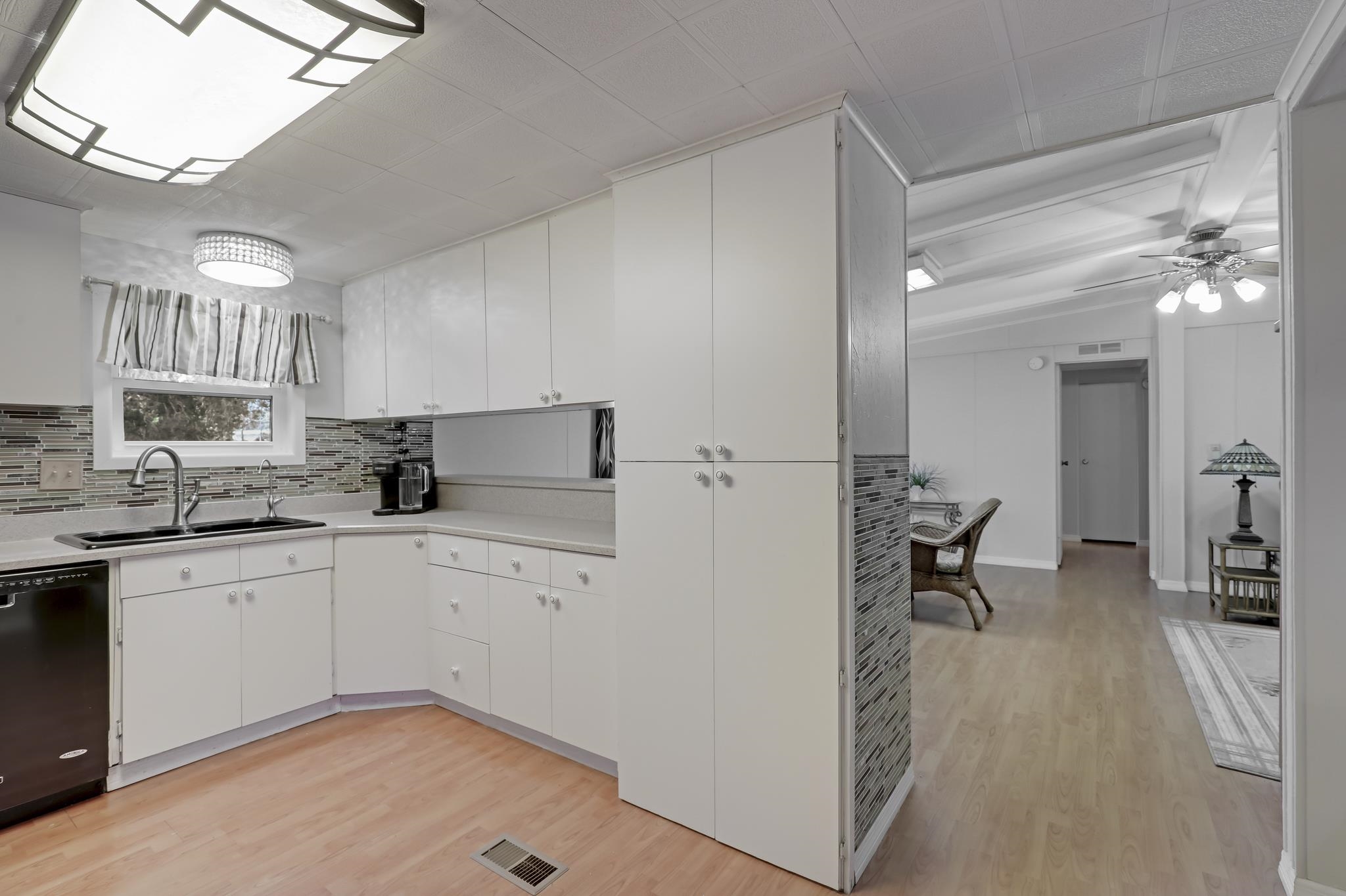 6901 Catlett Road St. Augustine, FL 32095 - Photo 32 of 74 Kitchen with light countertops, light wood-type flooring, black dishwasher, white cabinetry, and tasteful backsplash