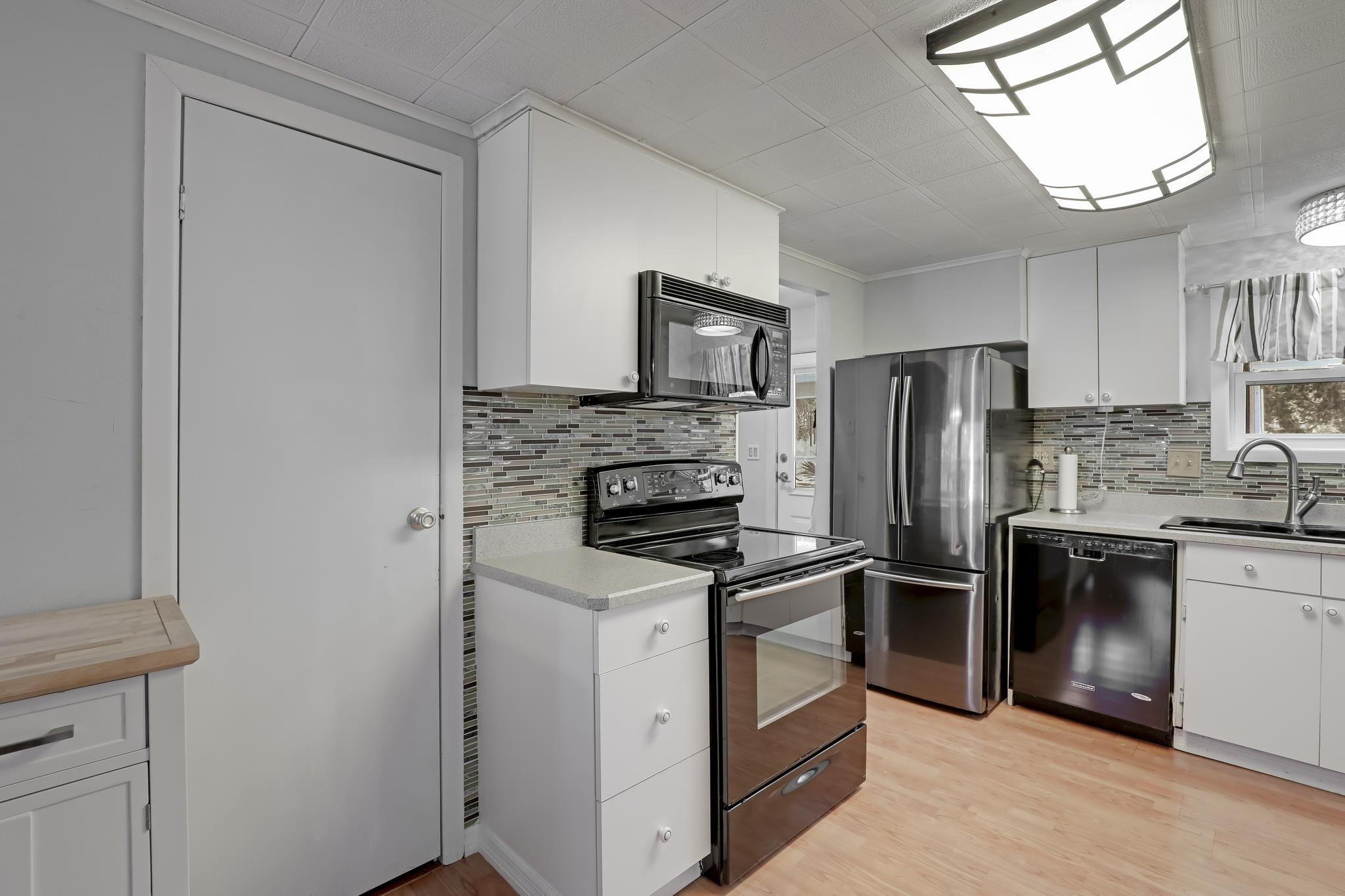 6901 Catlett Road St. Augustine, FL 32095 - Photo 33 of 74 Kitchen featuring white cabinets, black appliances, light wood-style floors, and crown molding
