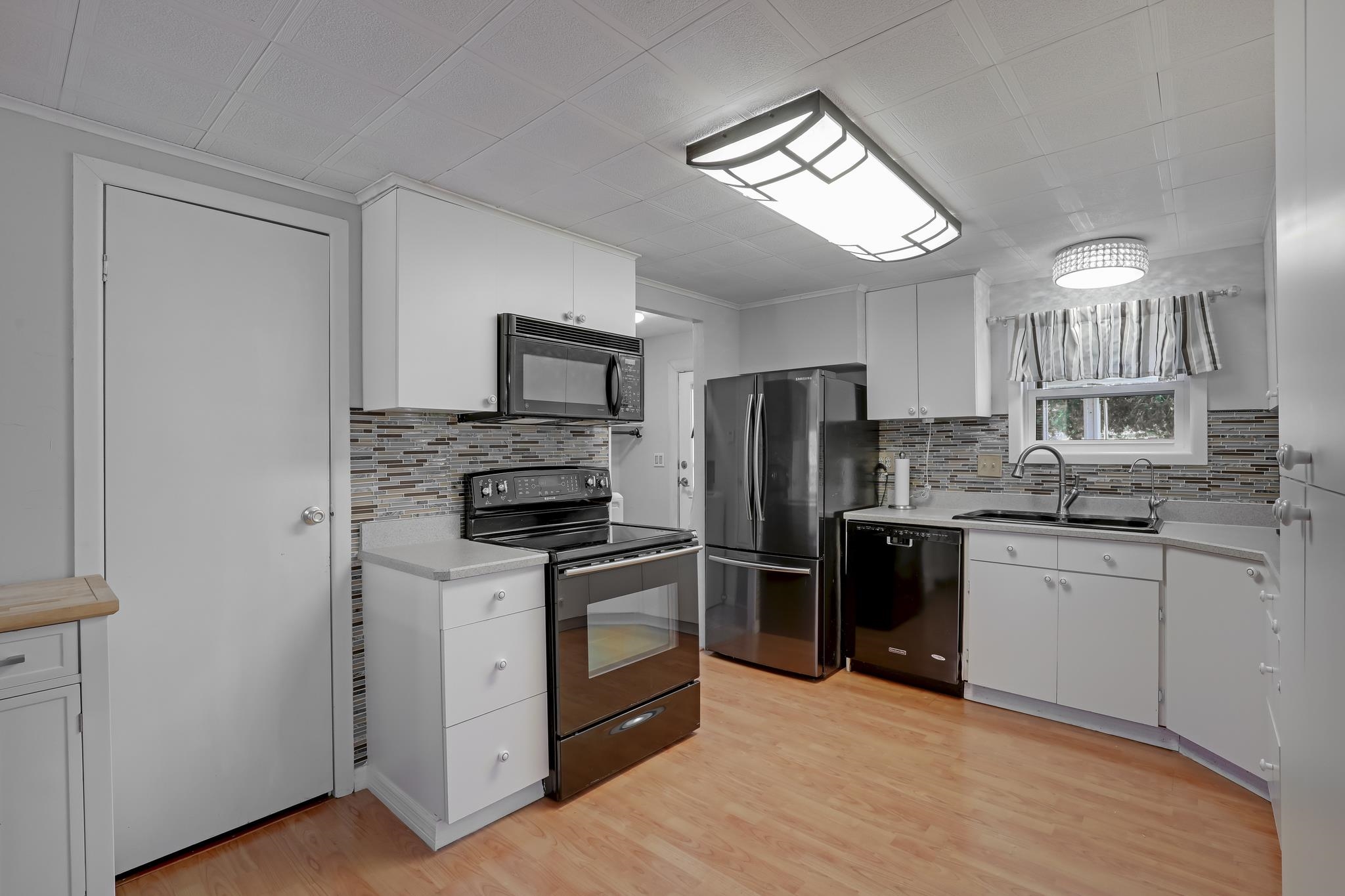 6901 Catlett Road St. Augustine, FL 32095 - Photo 4 of 74 Kitchen featuring white cabinets, black appliances, light wood-type flooring, crown molding, and decorative backsplash