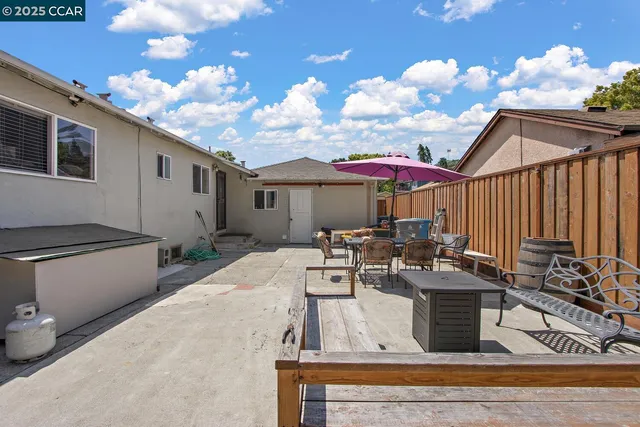 a view of a patio with couches table and chairs under an umbrella with wooden fence