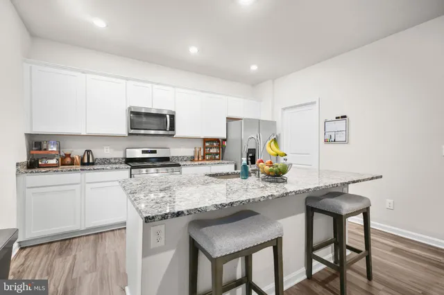 a kitchen with stainless steel appliances granite countertop a stove top oven a sink a refrigerator white cabinets and wooden floor