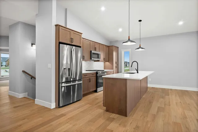 a kitchen with stainless steel appliances granite countertop a refrigerator a sink dishwasher a kitchen island with wooden floor and cabinets
