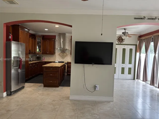 a living room with stainless steel appliances furniture a flat screen tv and a kitchen view