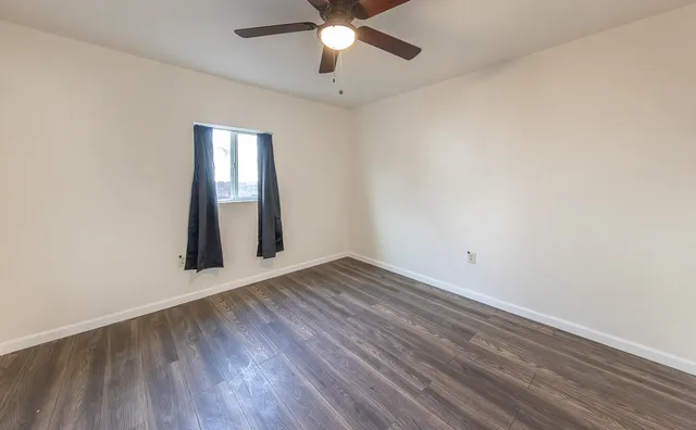 an empty room with wooden floor chandelier fan and windows